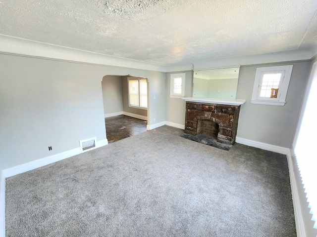 unfurnished living room featuring a stone fireplace, arched walkways, visible vents, and a wealth of natural light