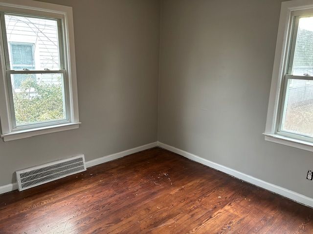 spare room featuring dark wood-type flooring, baseboards, visible vents, and a wealth of natural light