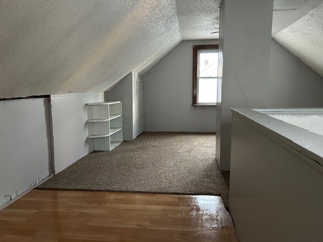 additional living space with vaulted ceiling, wood finished floors, and a textured ceiling