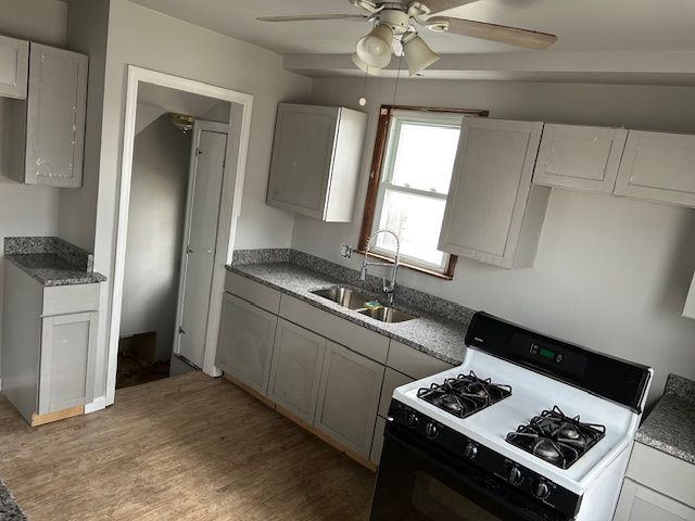 kitchen with ceiling fan, gas range oven, light wood-type flooring, and a sink