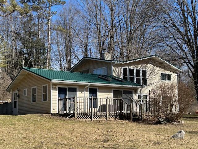 rear view of property featuring a deck, metal roof, and a yard