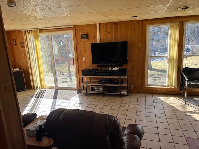 living room featuring light tile patterned floors, a drop ceiling, and wood walls