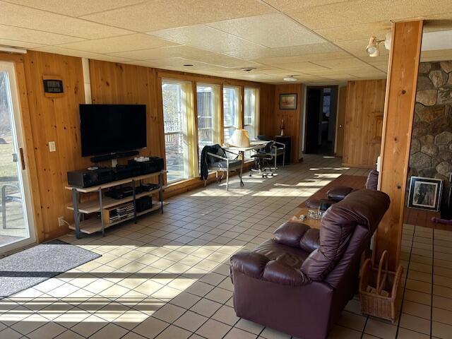 living room featuring a drop ceiling, light tile patterned floors, and wood walls