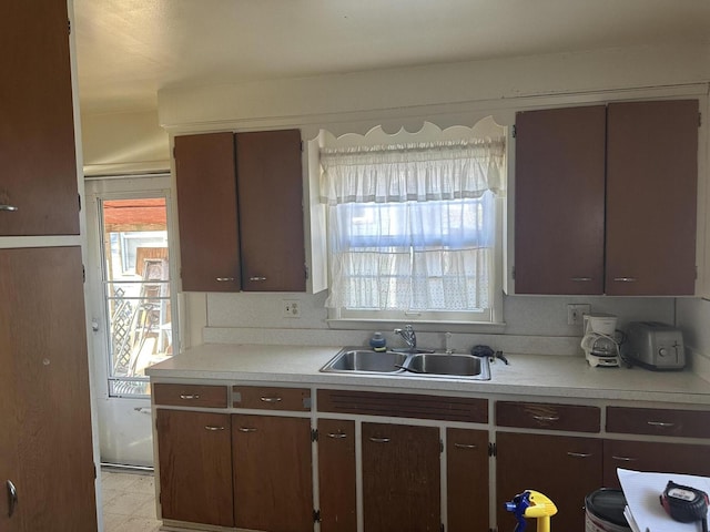 kitchen with light countertops, dark brown cabinets, light floors, and a sink