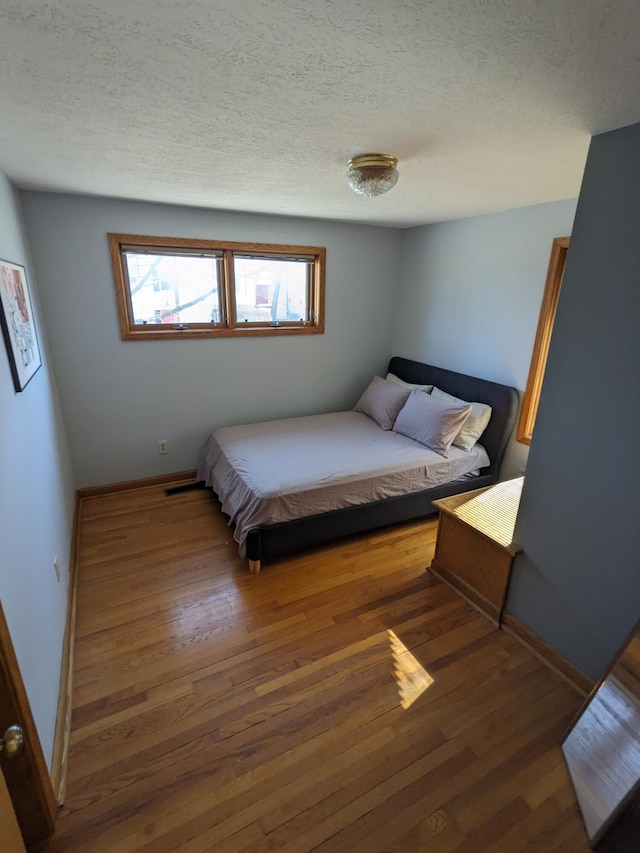 bedroom featuring visible vents, a textured ceiling, baseboards, and wood-type flooring