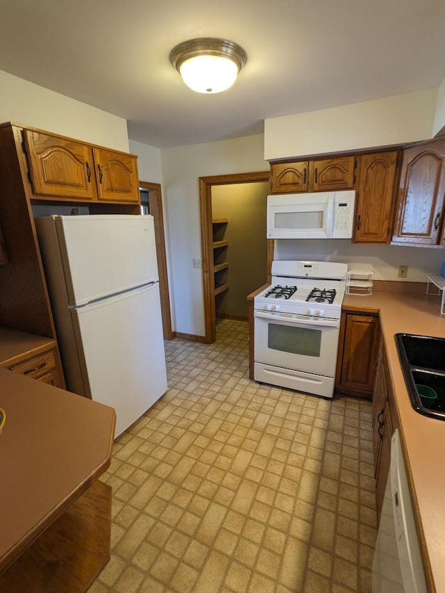 kitchen featuring a sink, baseboards, white appliances, and brown cabinets