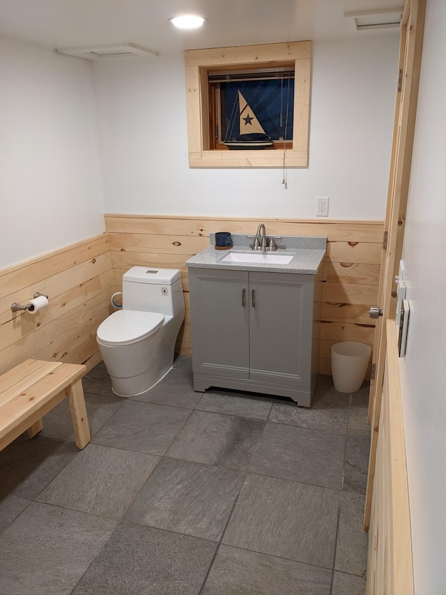 half bath featuring a wainscoted wall, vanity, toilet, and wooden walls