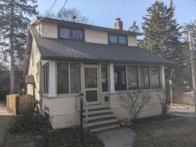 view of front of property with entry steps, a sunroom, roof with shingles, and a chimney