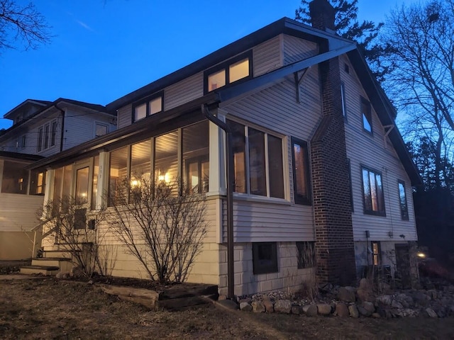 view of property exterior with driveway, a chimney, and a sunroom