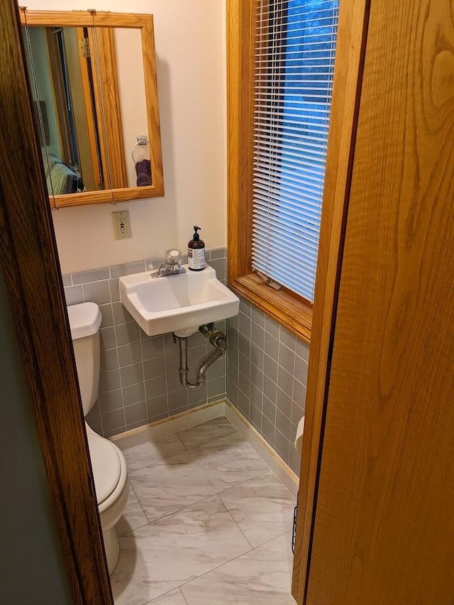 bathroom featuring marble finish floor, toilet, tile walls, and a sink