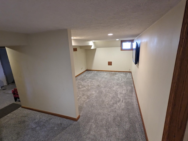 basement with a textured ceiling, baseboards, and carpet floors