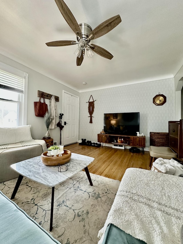 living area featuring wallpapered walls, wood finished floors, baseboards, and a ceiling fan