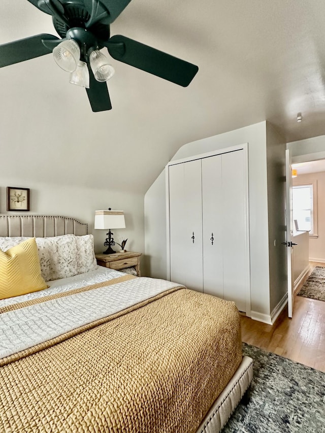 bedroom featuring baseboards, lofted ceiling, wood finished floors, a closet, and a ceiling fan