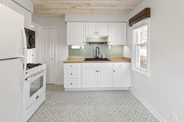 kitchen with a sink, baseboards, white appliances, and white cabinets