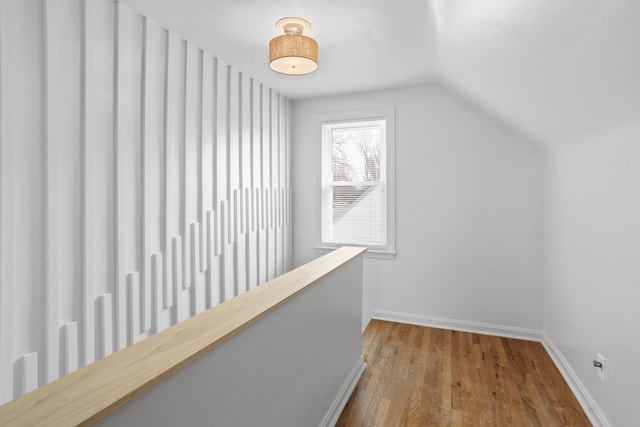 hall with baseboards, wood finished floors, and vaulted ceiling