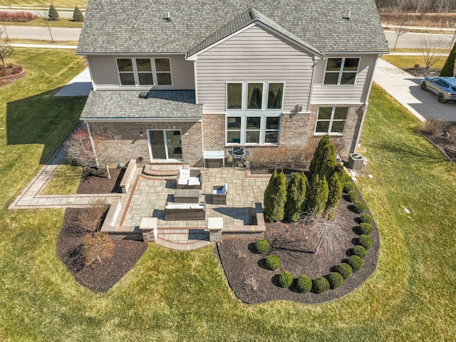 back of house with a patio, a yard, roof with shingles, outdoor lounge area, and brick siding