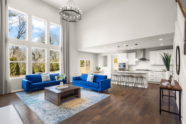 living area with a notable chandelier, dark wood-style floors, recessed lighting, and a towering ceiling