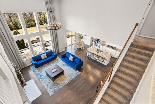 living room with a notable chandelier, wood finished floors, stairway, a high ceiling, and baseboards