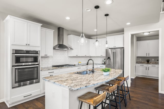 kitchen with dark wood-style floors, stainless steel appliances, a sink, white cabinets, and wall chimney exhaust hood