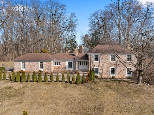 back of house with brick siding, a lawn, a chimney, and a fenced front yard