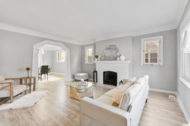 living area featuring visible vents, baseboards, a fireplace with flush hearth, arched walkways, and light wood-style floors