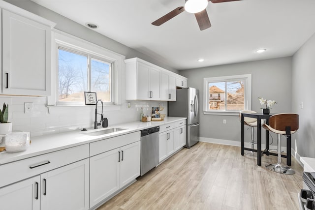 kitchen with a sink, appliances with stainless steel finishes, light wood-style flooring, and white cabinetry