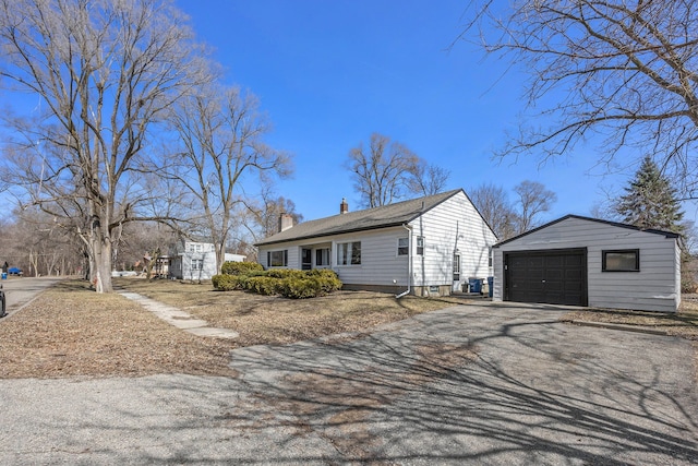 view of front of home featuring a garage, a chimney, an outdoor structure, and driveway