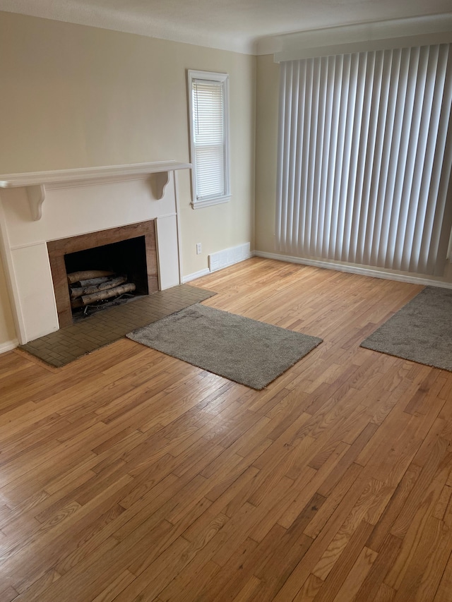 unfurnished living room with a tiled fireplace, visible vents, baseboards, and hardwood / wood-style flooring