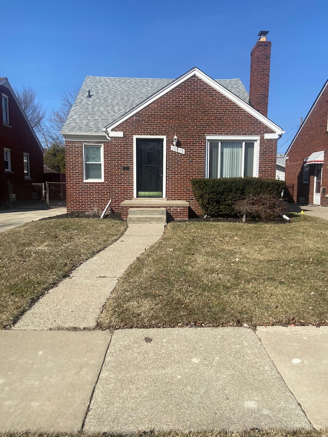 view of front facade with a front lawn, brick siding, roof with shingles, and a chimney