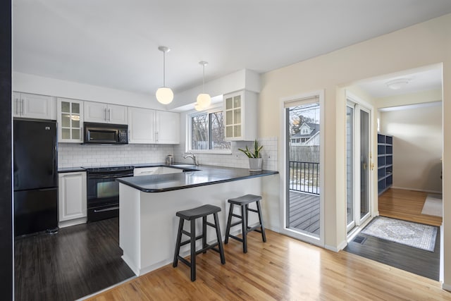 kitchen with a kitchen bar, black appliances, a sink, dark countertops, and a peninsula