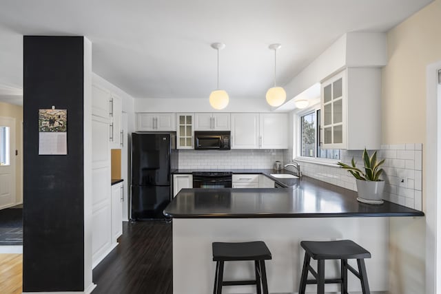 kitchen with dark wood finished floors, a peninsula, black appliances, white cabinetry, and dark countertops