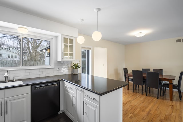 kitchen featuring dark countertops, dishwasher, decorative backsplash, a peninsula, and a sink