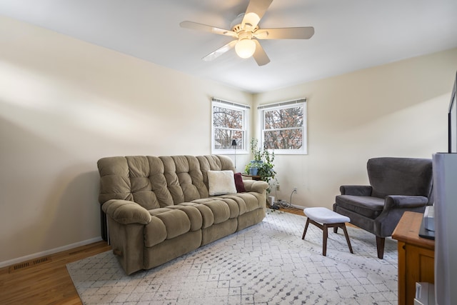 living room featuring a ceiling fan, baseboards, visible vents, and light wood finished floors