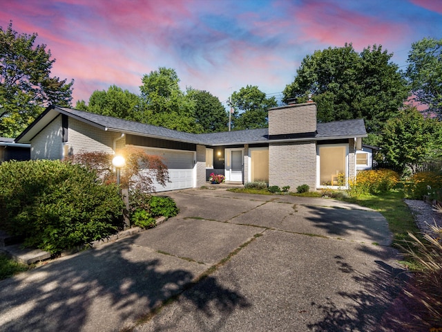 view of front of property featuring driveway, roof with shingles, a garage, brick siding, and a chimney