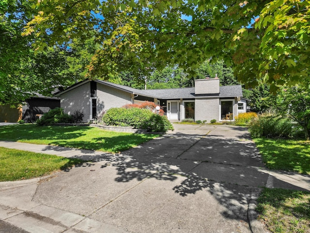 mid-century inspired home with a front lawn, brick siding, driveway, and a chimney