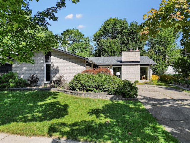 mid-century home featuring brick siding, a chimney, and a front lawn