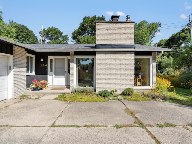 property entrance with brick siding, roof with shingles, and a chimney