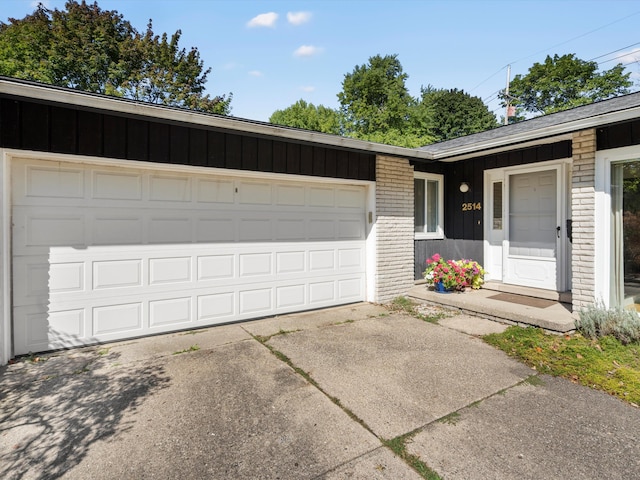 view of front of property featuring board and batten siding, an attached garage, brick siding, and driveway