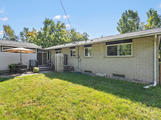 back of property with a patio, a yard, brick siding, and crawl space