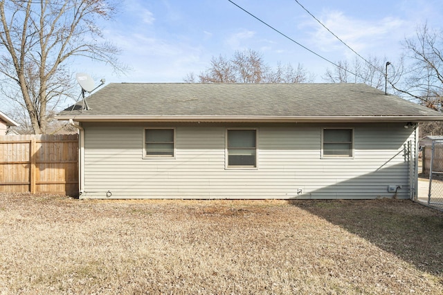 rear view of house featuring roof with shingles and fence