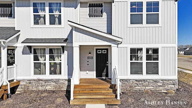 doorway to property with board and batten siding, stone siding, and roof with shingles