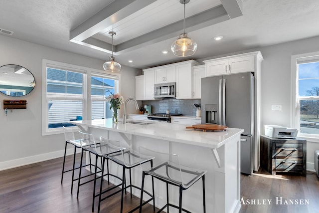 kitchen featuring backsplash, white cabinets, stainless steel appliances, a raised ceiling, and a kitchen island with sink