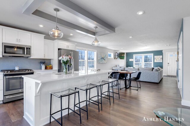 kitchen featuring dark wood-type flooring, a center island with sink, white cabinetry, stainless steel appliances, and decorative backsplash