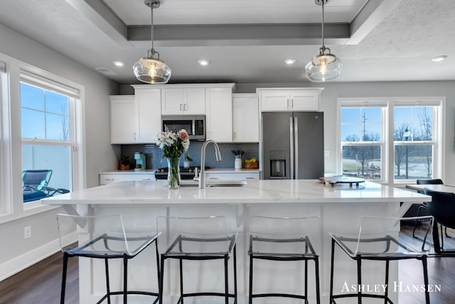 kitchen with dark wood finished floors, a tray ceiling, a sink, stainless steel appliances, and backsplash