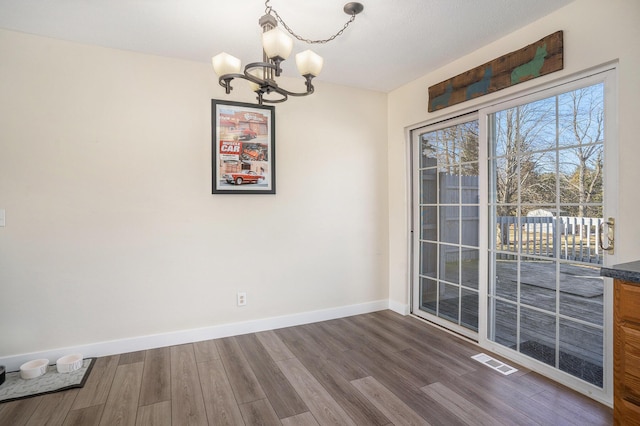 unfurnished dining area featuring a notable chandelier, visible vents, baseboards, and dark wood-style flooring