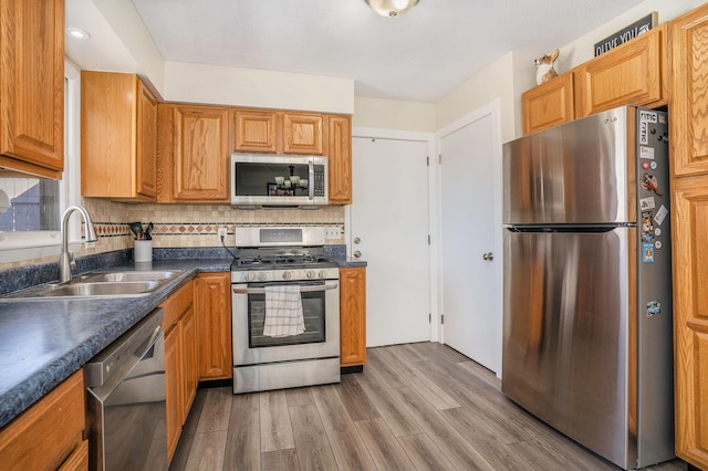 kitchen with a sink, tasteful backsplash, dark countertops, stainless steel appliances, and light wood finished floors