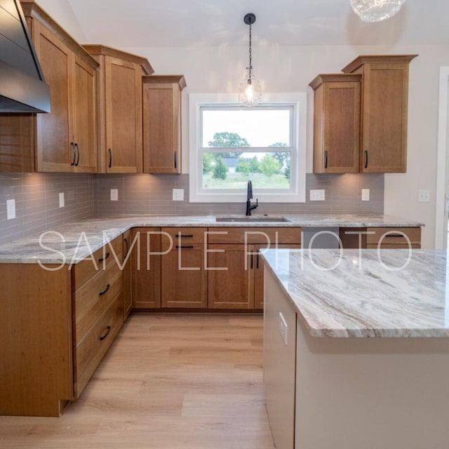 kitchen with brown cabinetry, range hood, tasteful backsplash, and a sink