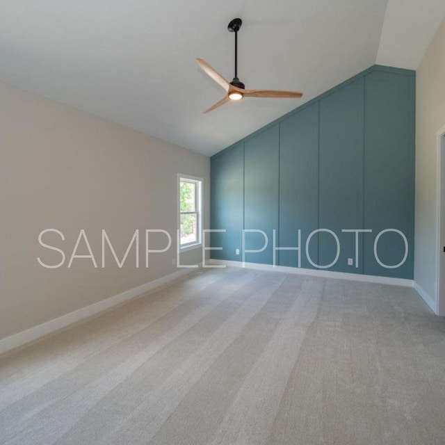 spare room featuring lofted ceiling, carpet flooring, a decorative wall, baseboards, and ceiling fan