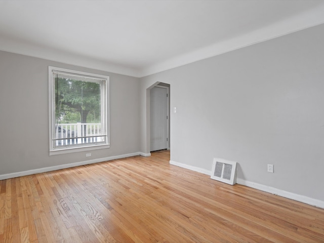 spare room with light wood-style floors, arched walkways, visible vents, and baseboards