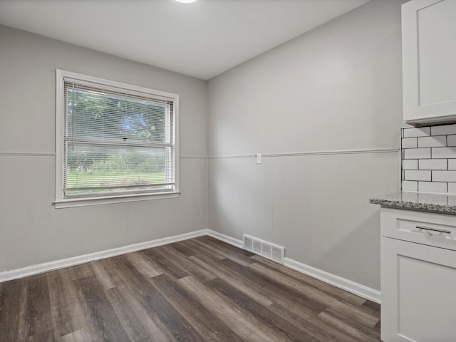 unfurnished dining area featuring dark wood-type flooring, baseboards, and visible vents